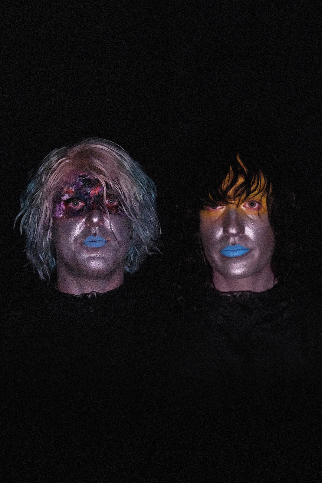 Close up portrait of Will Weisenfeld and Jesse Clark in distored chrome makeup and bright blue lips against a black backdrop